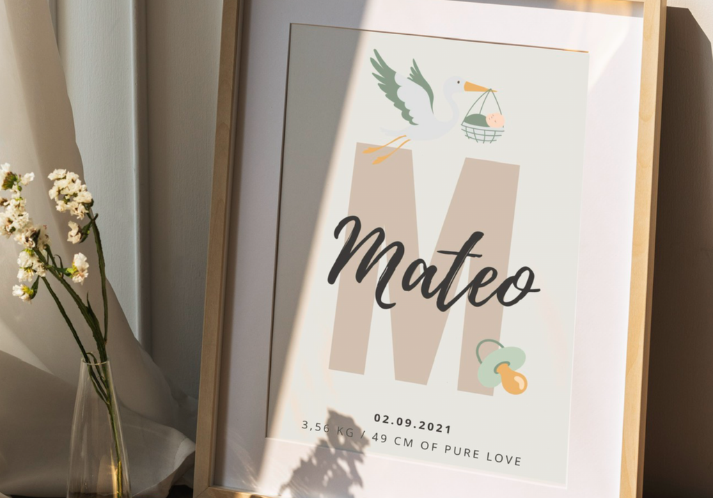 Framed baby milestone card with 'Mateo' and stork illustration, placed on a surface.