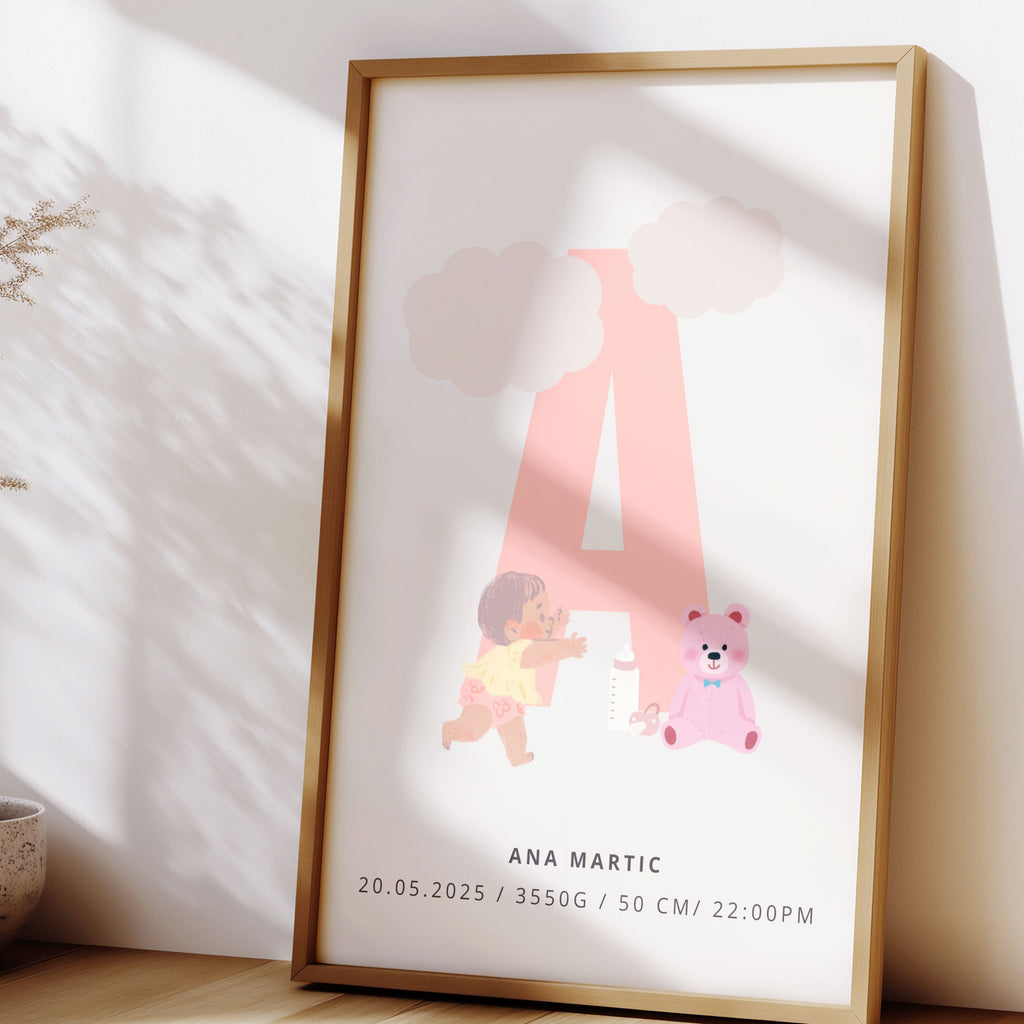 Framed artwork with a pink letter 'A' and small illustrations on a white background, placed on a wooden surface with a vase and plants in the background.